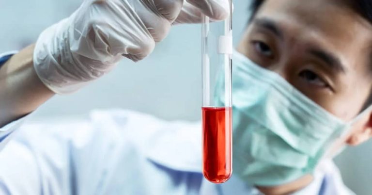 A toxicologist in a lab coat and surgical mask examines a test tube containing a red substance, reflecting the diverse roles in toxicology.